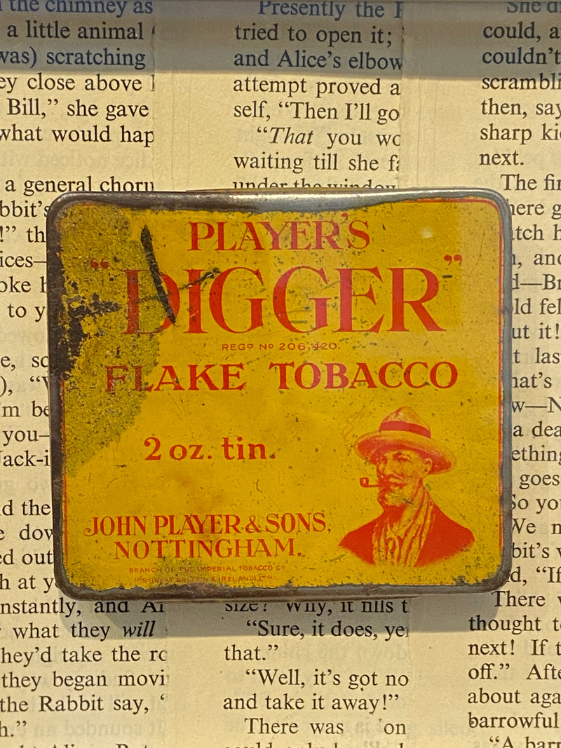 Vintage ‘Players Digger Flake Tobacco’ tin framed with vintage Alice in Wonderland book text. By Lost and Found Projects.
