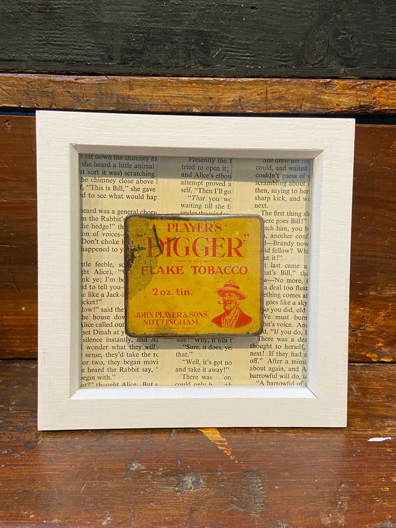 Vintage ‘Players Digger Flake Tobacco’ tin framed with vintage Alice in Wonderland book text. By Lost and Found Projects.